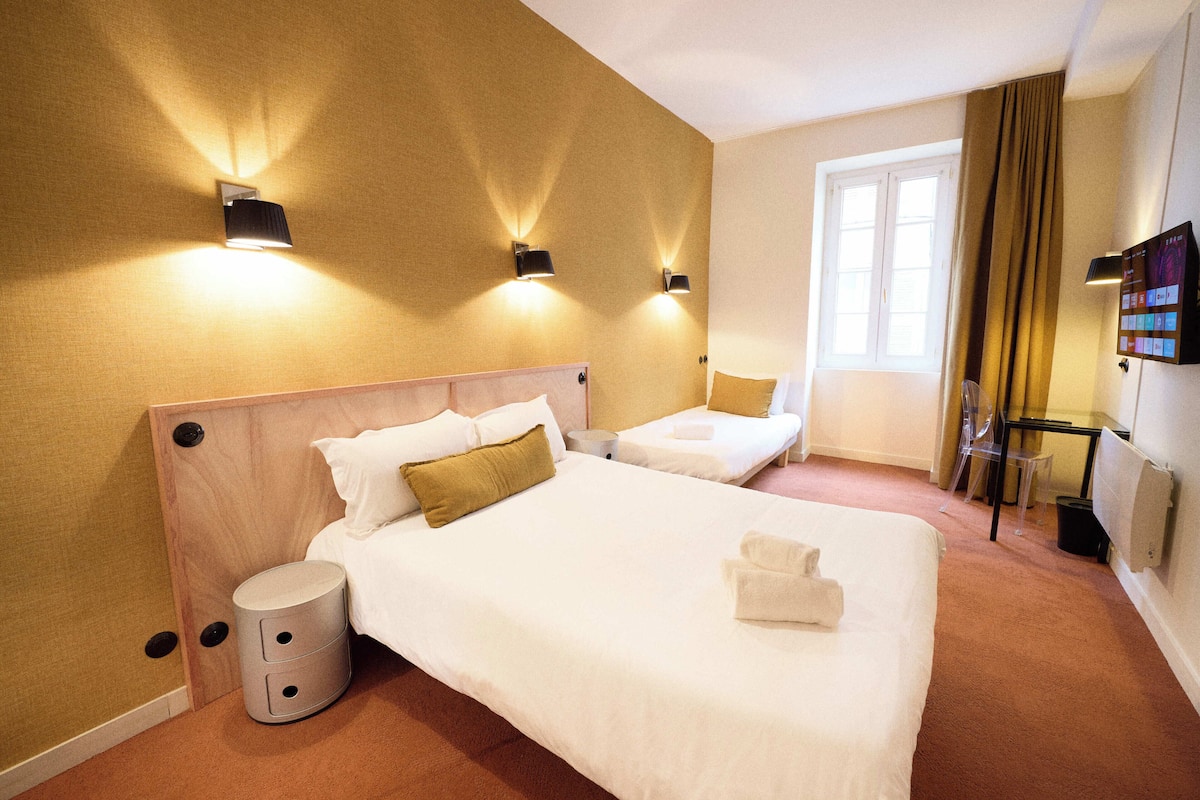 Habitación de hotel con una cama grande, una cama más pequeña, una mesita de noche, una lámpara, un televisor y un ventanal con cortinas.