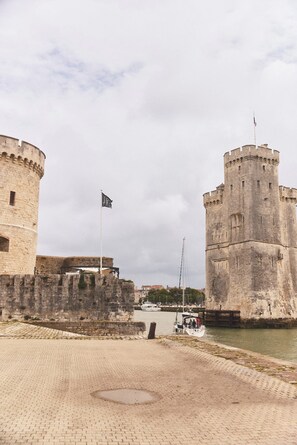 Un castillo de piedra histórico con una bandera, un paseo marítimo empedrado y un barco amarrado cerca.