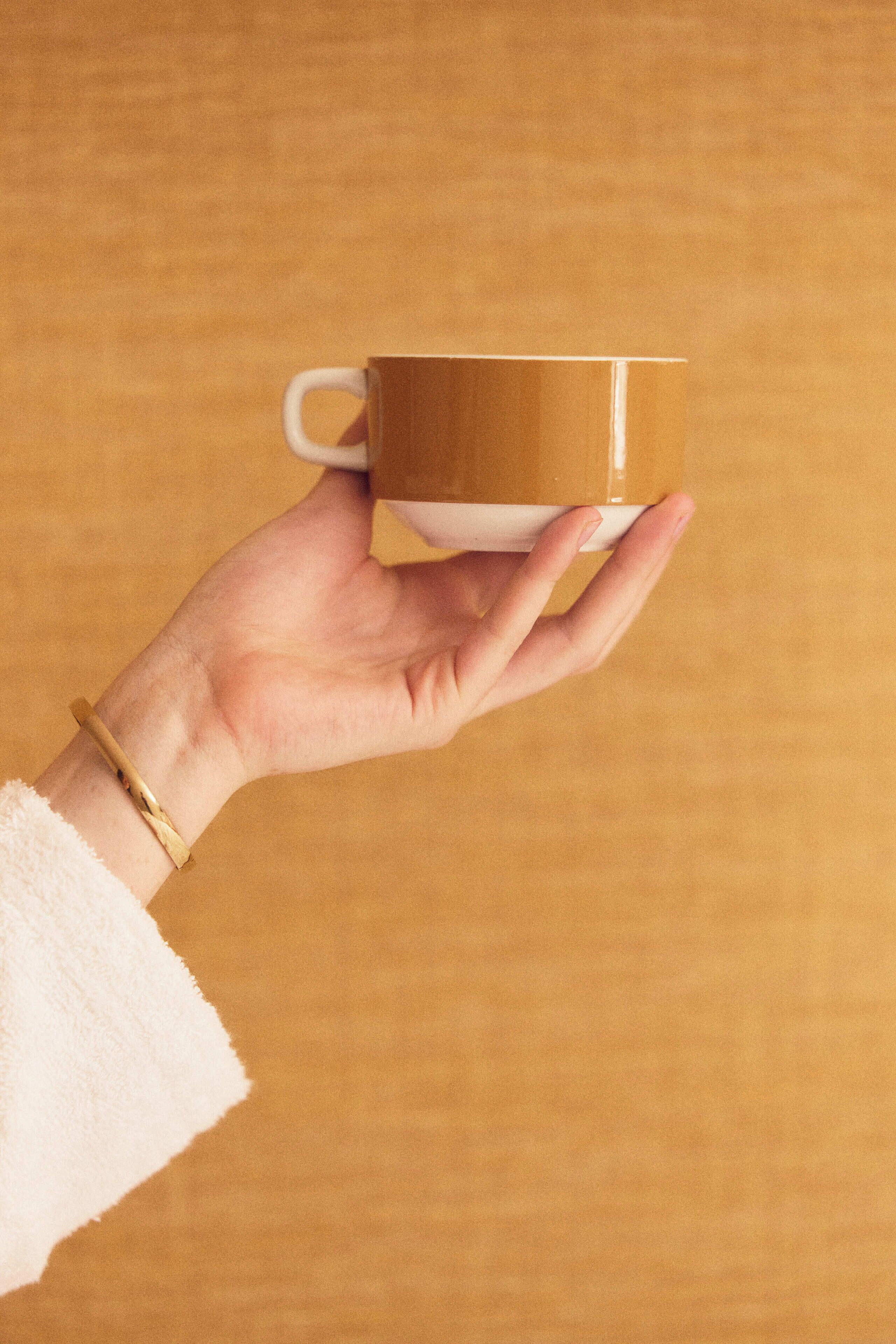 A hand holding a cup against a wooden background.