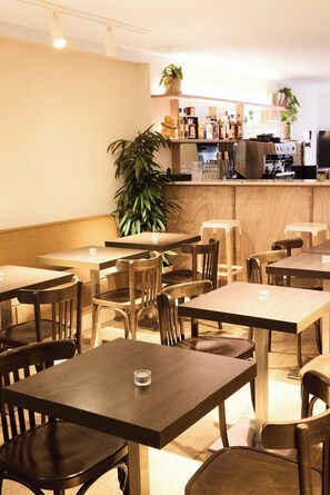 A restaurant interior with wooden tables and chairs, a counter with a coffee machine, and potted plants. - Hotel Henri IV (La Rochelle)