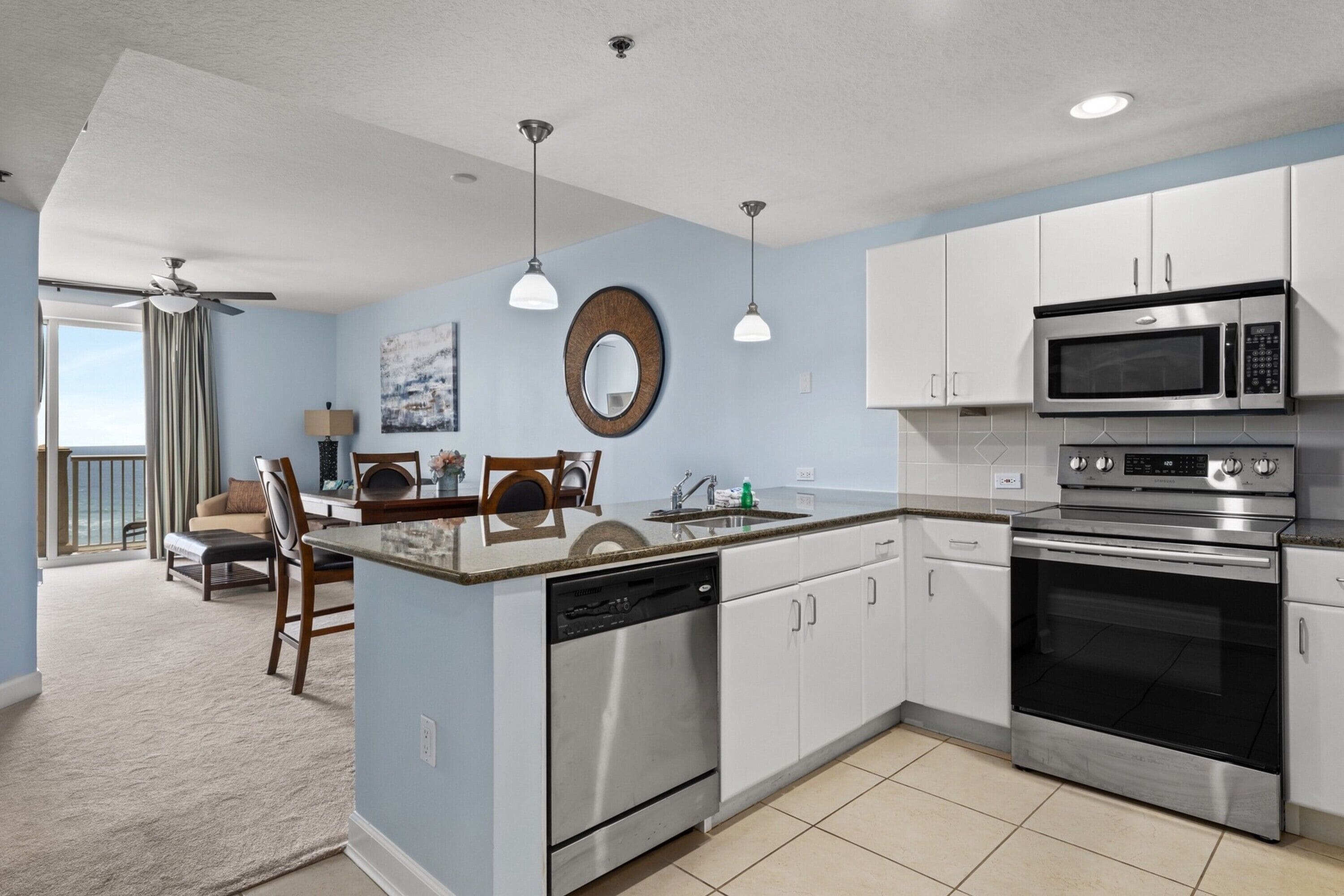 A modern kitchen with white cabinets, stainless steel appliances, and a dining area with a view.