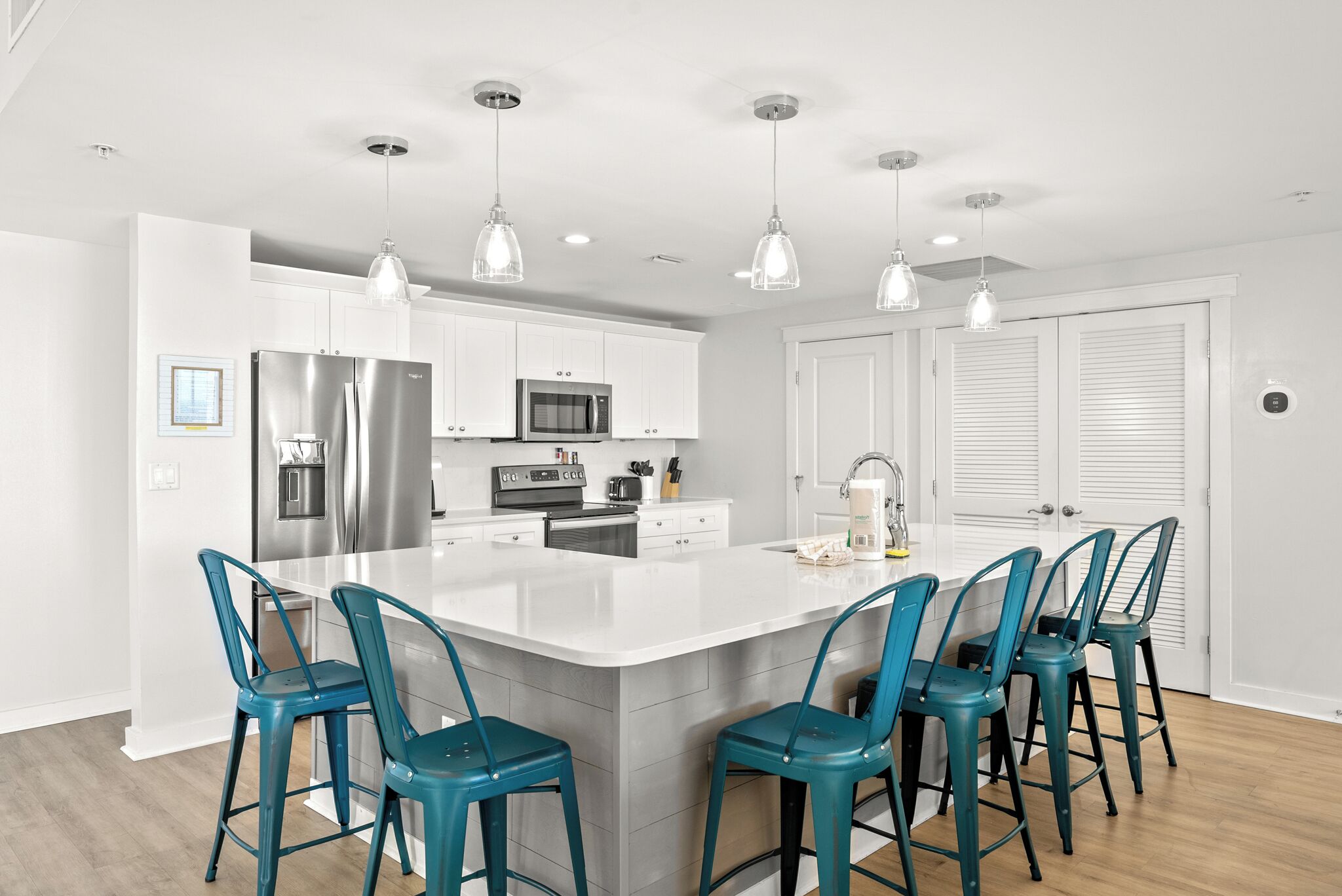 Una cocina moderna con una isla central, electrodomésticos de acero inoxidable y taburetes de bar color turquesa.
