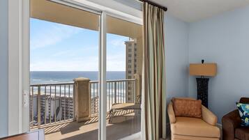 A balcony with a view of the ocean and buildings, a chair, a lamp, and a door with a sign.