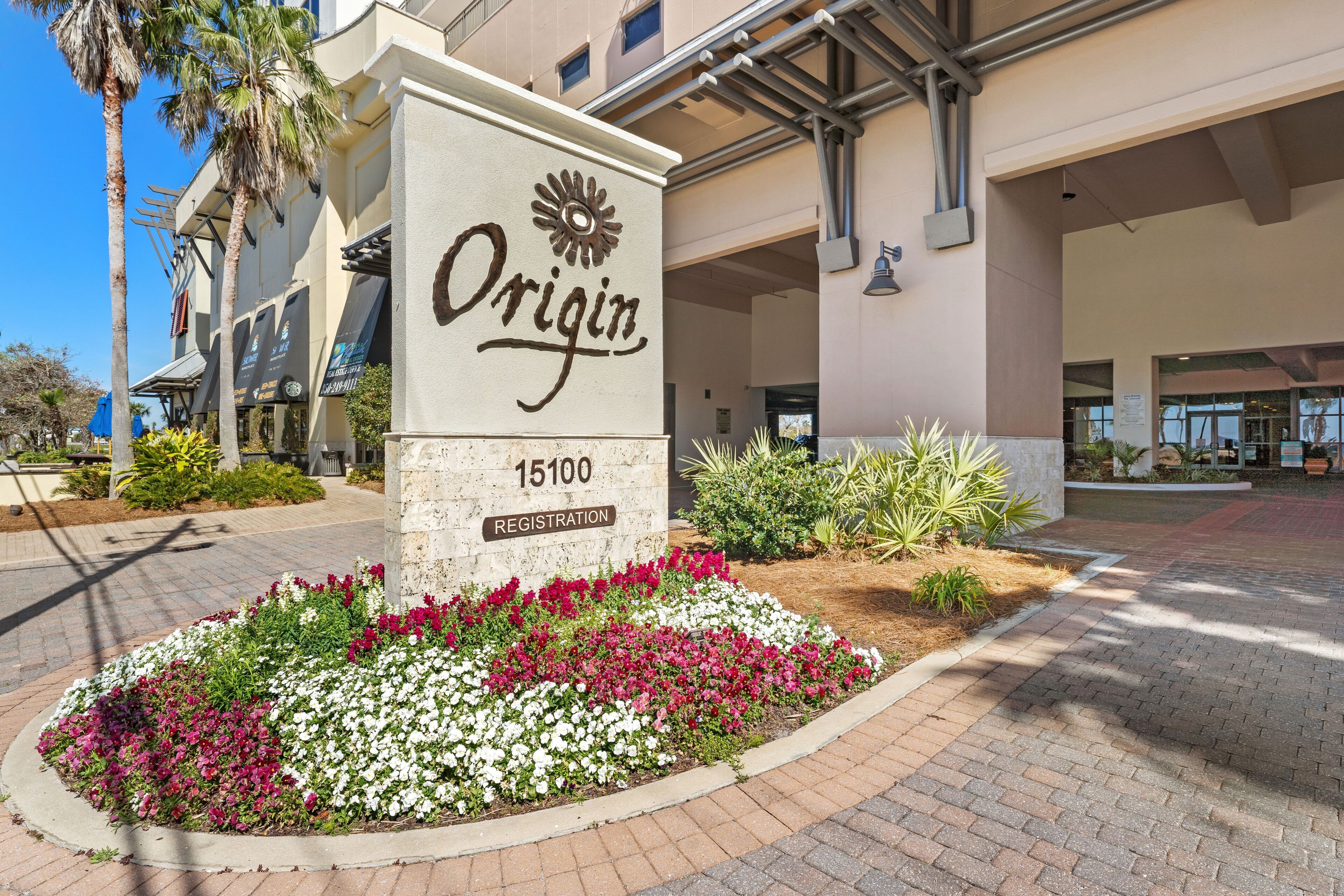 Ein Hotel Eingang mit einem Schild, auf dem 'Origin 15100 Registration' steht, umgeben von einem Blumenbeet.