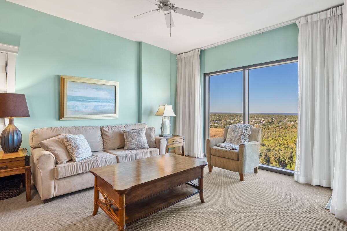 A spacious living room with a large window offering a scenic view, a ceiling fan, and a cozy seating area.