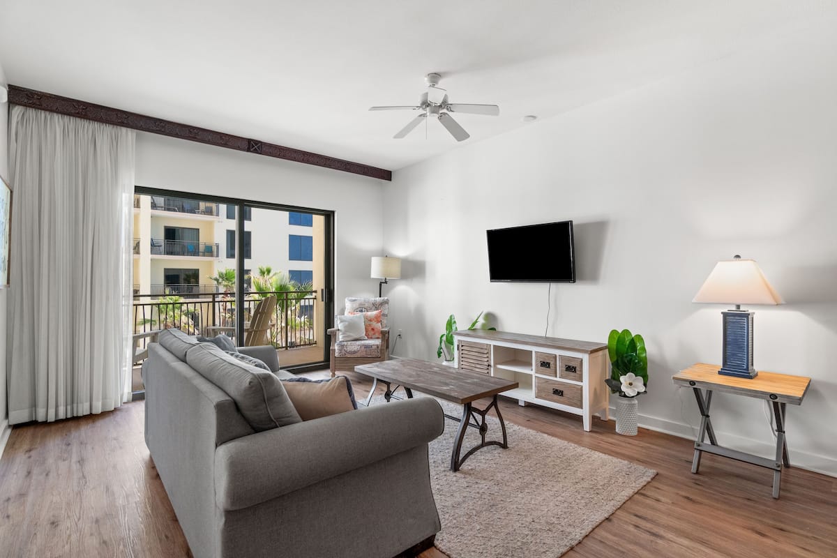 A modern living room with a sofa, coffee table, TV, and a balcony with a view of buildings.
