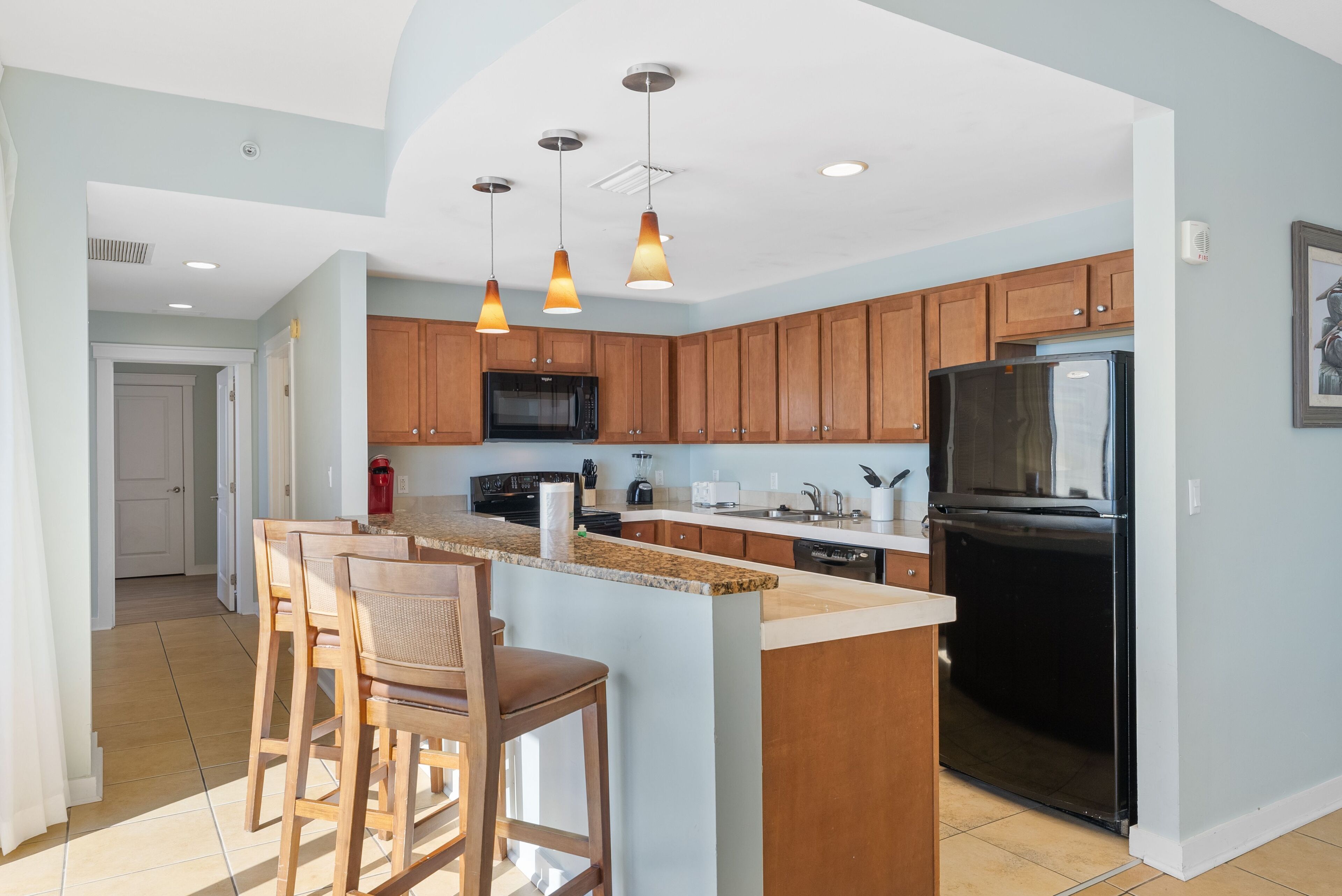 A modern kitchen with wooden cabinets, a black refrigerator, and a granite countertop.