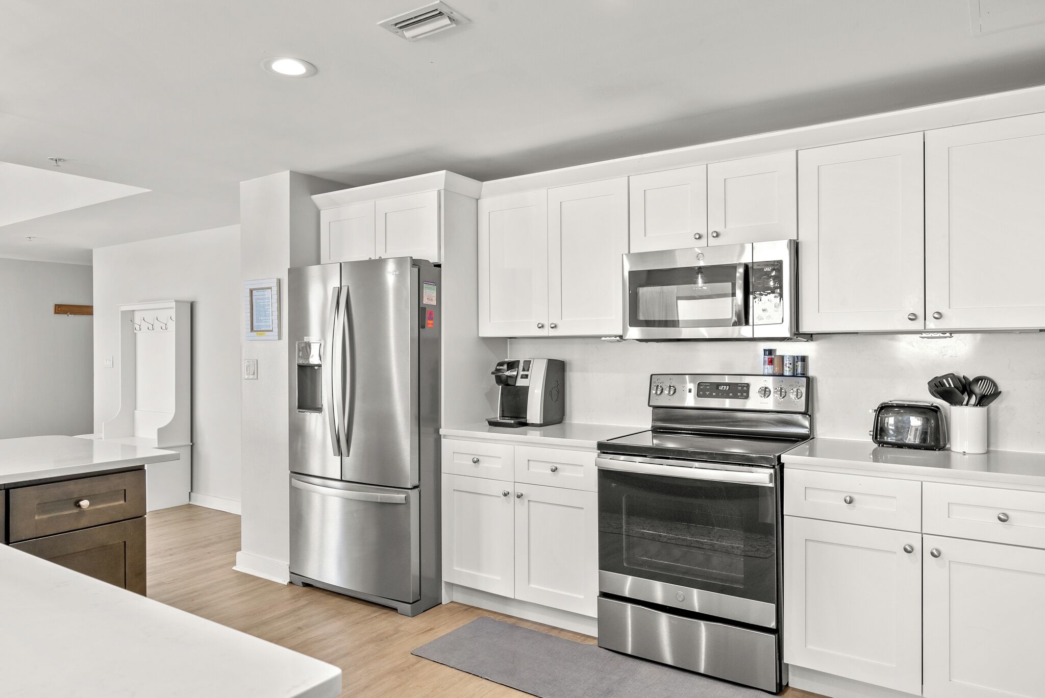 A modern kitchen with stainless steel appliances, white cabinetry, and a grey rug.