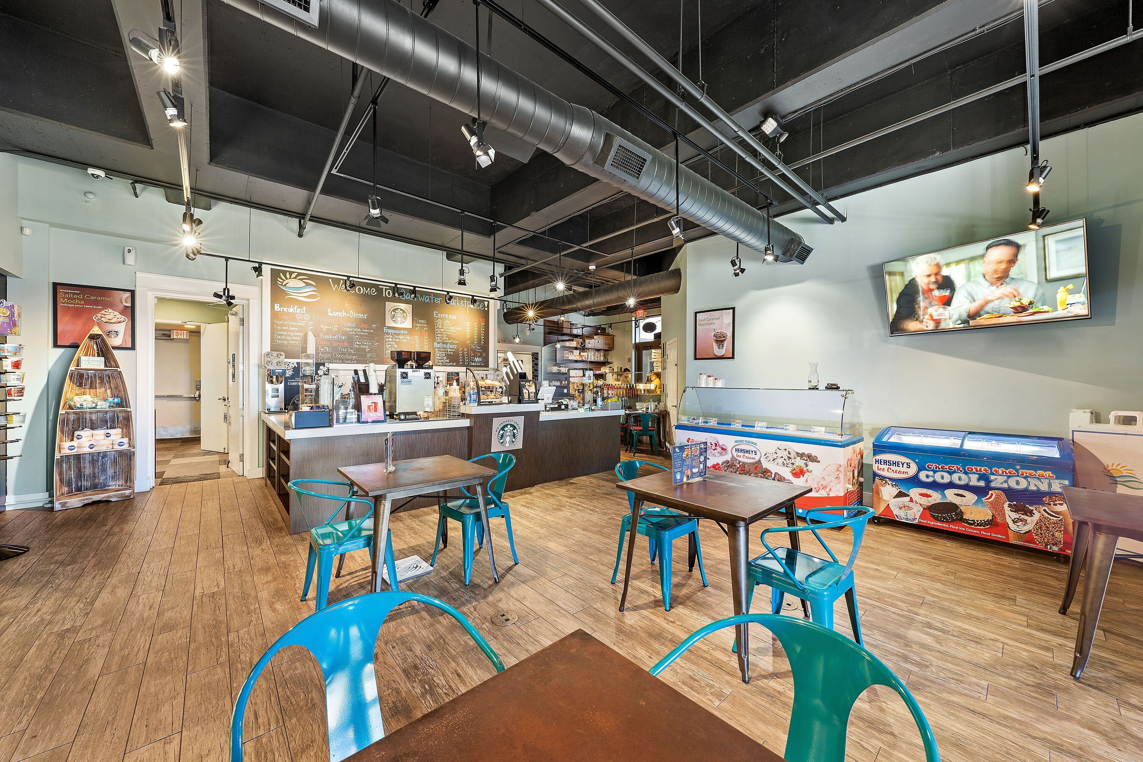 Un café con piso de madera, sillas azules, una barra con menú y una exhibición de helados Hershey's.