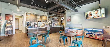 A café with wooden flooring, blue chairs, a counter with a menu, and a Hershey's ice cream display.
