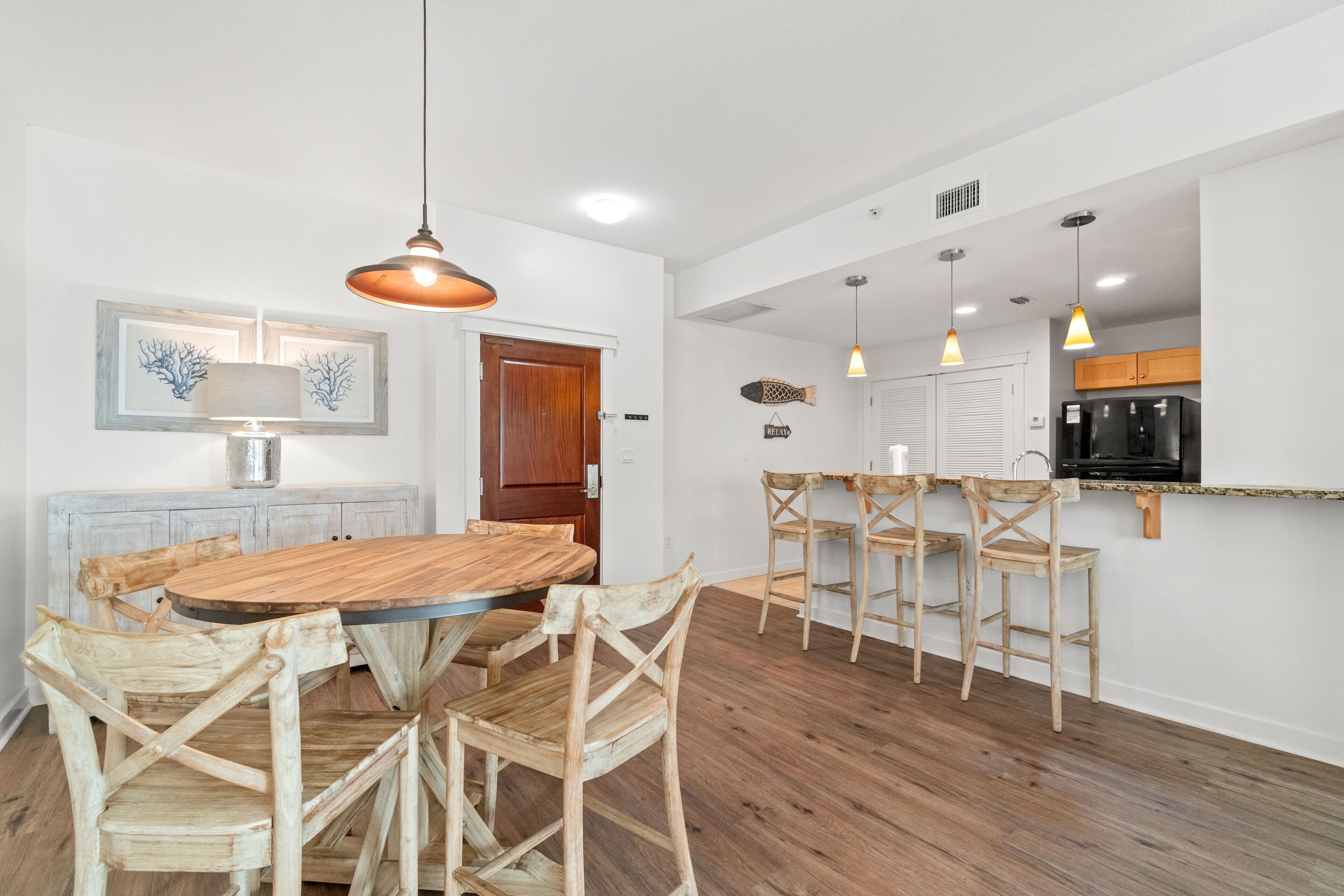 Eine moderne Küche mit Holztisch, Stühlen, Pendelleuchten und einem schwarzen Kühlschrank.