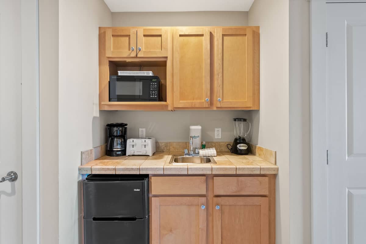 A compact kitchen with wooden cabinets, a black refrigerator, a microwave, a toaster, a coffee maker, and a blender.