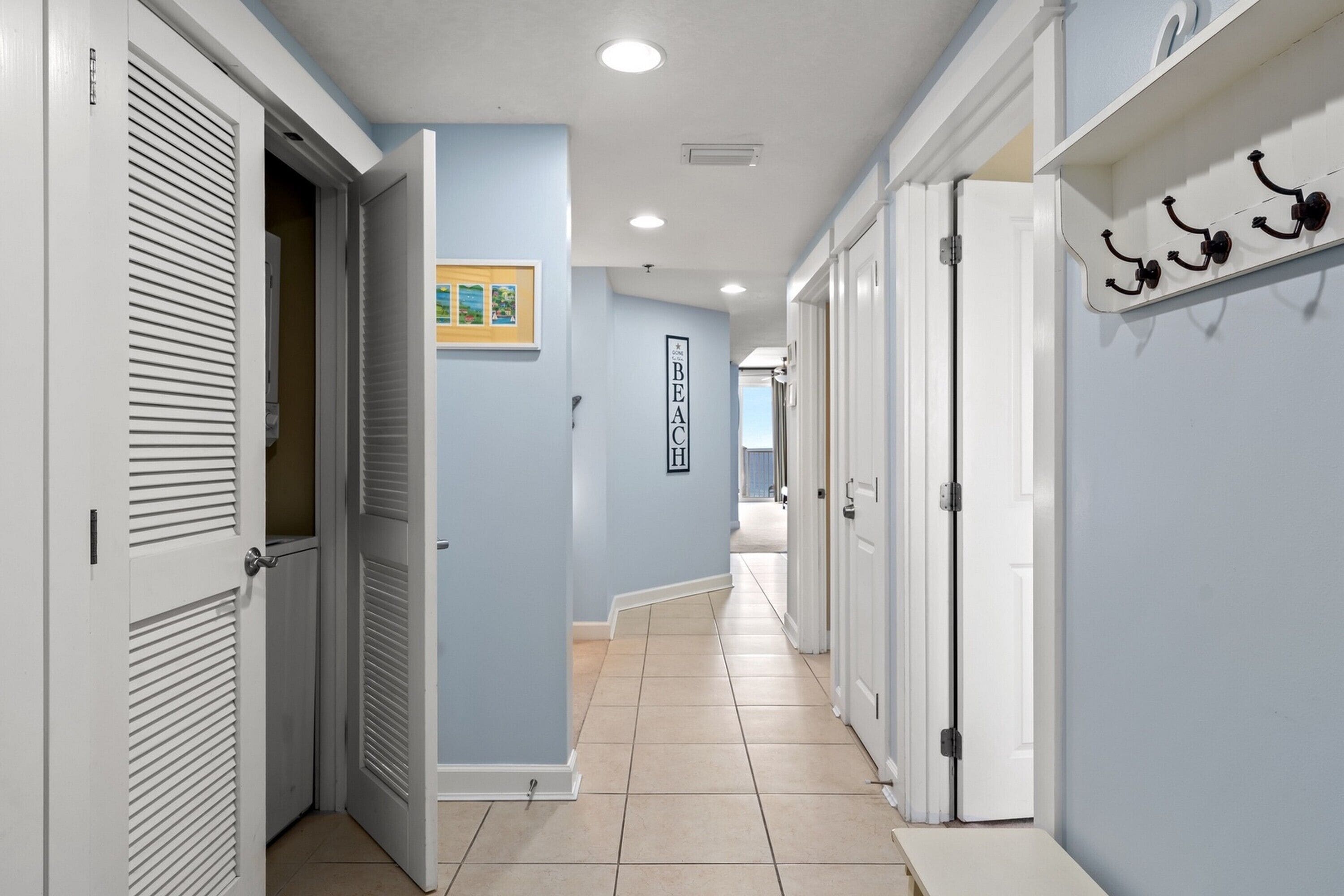 A hallway with white doors, a coat rack, and a sign reading "BEACH HOUSE".
