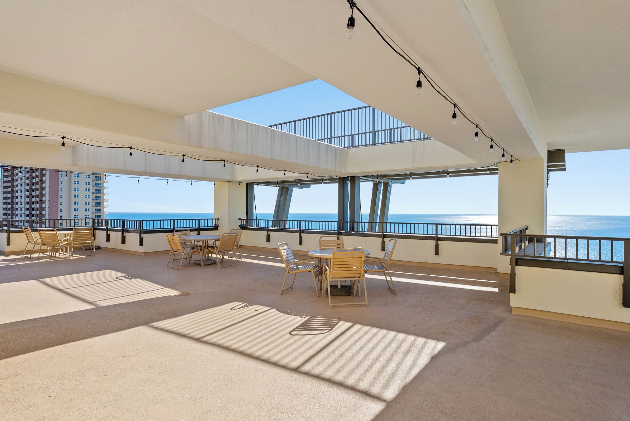 Un vaste espace intérieur doté d’un haut plafond, de grandes fenêtres et d’une vue sur l’océan. On y trouve plusieurs tables et chaises disposées pour les repas ou les moments de convivialité.