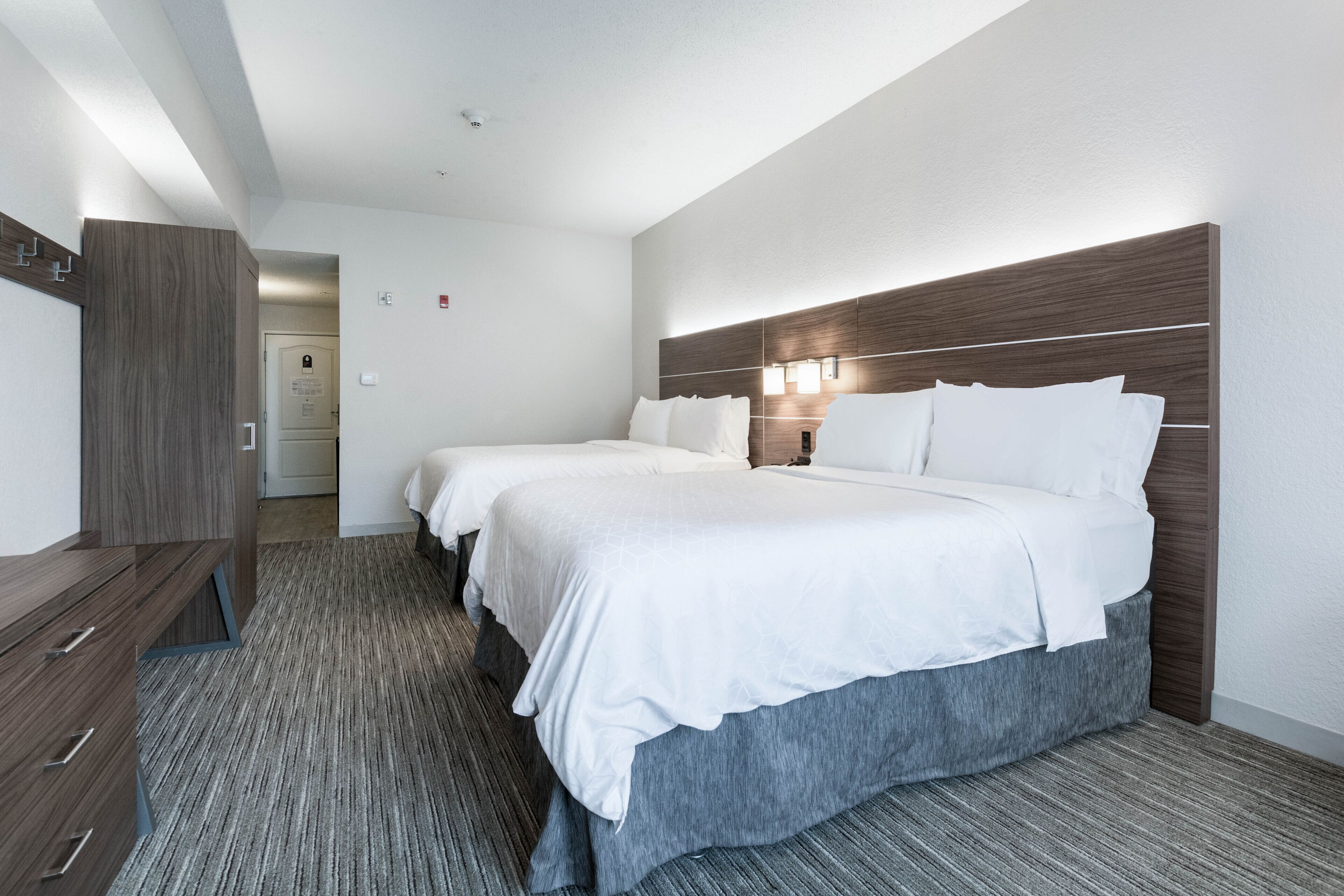 A hotel room with three beds, a wooden wardrobe, and a carpeted floor.
