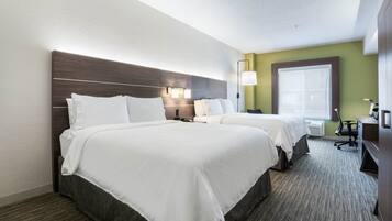 Ett hotellrum med två sängar, ett skrivbord, en stol, en lampa och ett fönster.