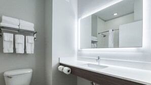 A modern bathroom with a white sink, mirror, and toilet. There are towels hanging on a rack and a roll of toilet paper on the wall.