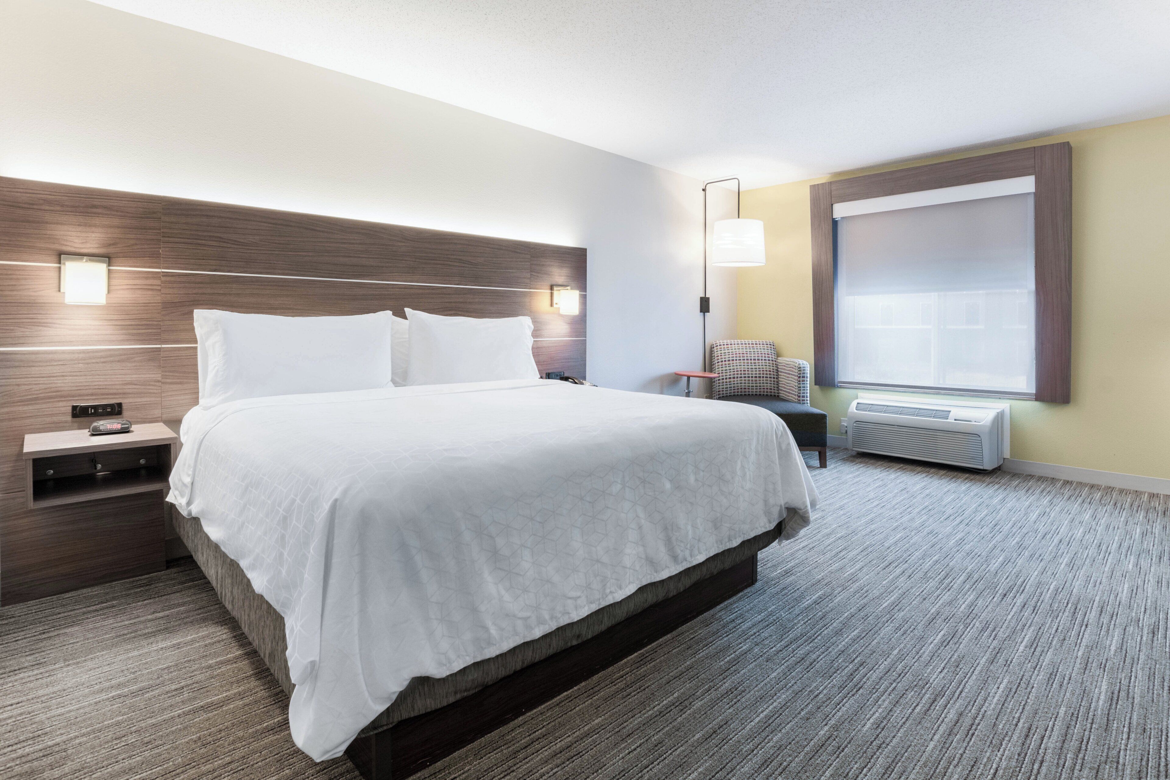 Une chambre d’hôtel avec un grand lit, des tables de chevet, une chaise, une fenêtre avec des stores et un radiateur fixé au mur.