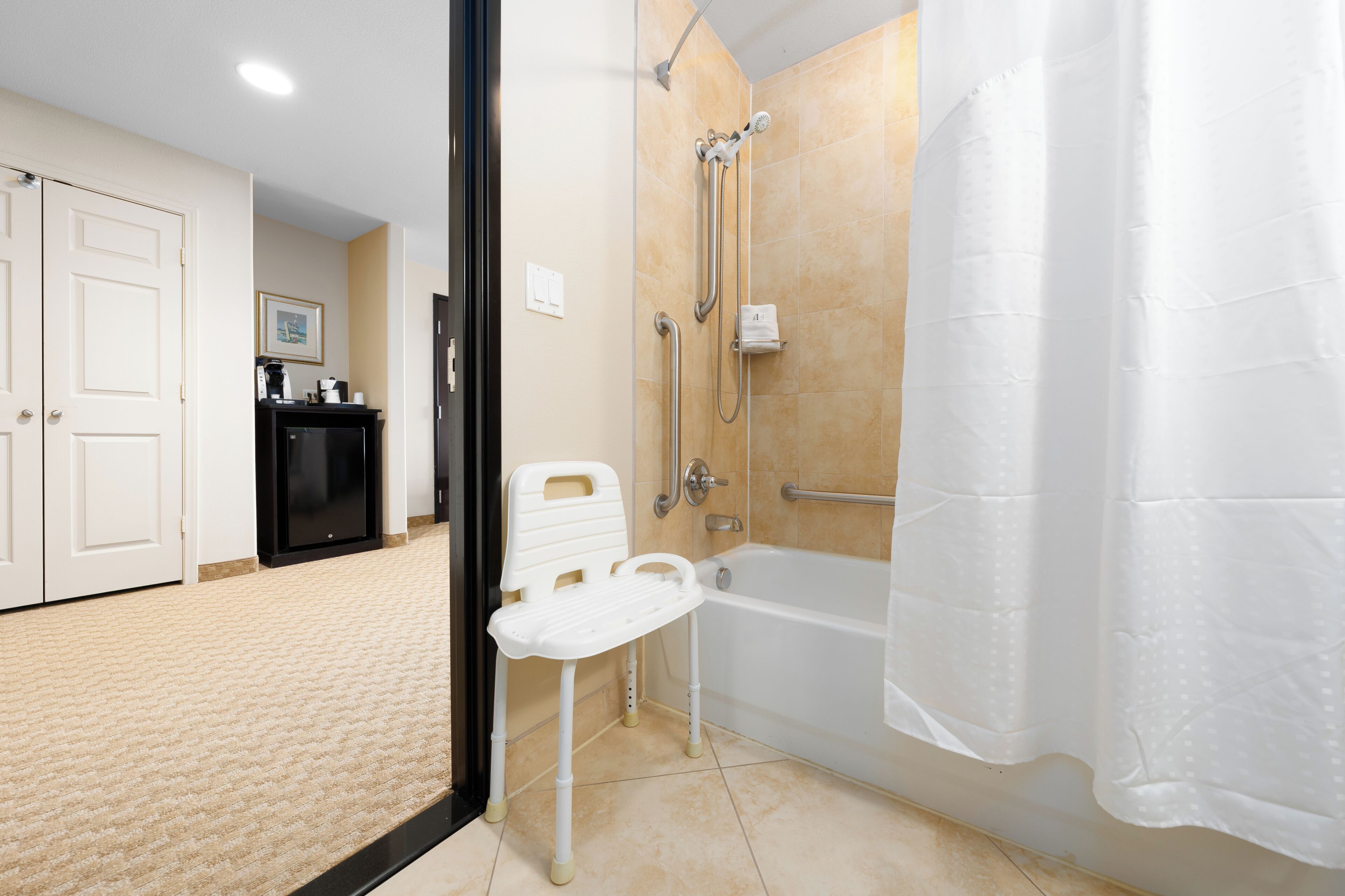 Un baño con ducha, bañera, una silla blanca y un inodoro.