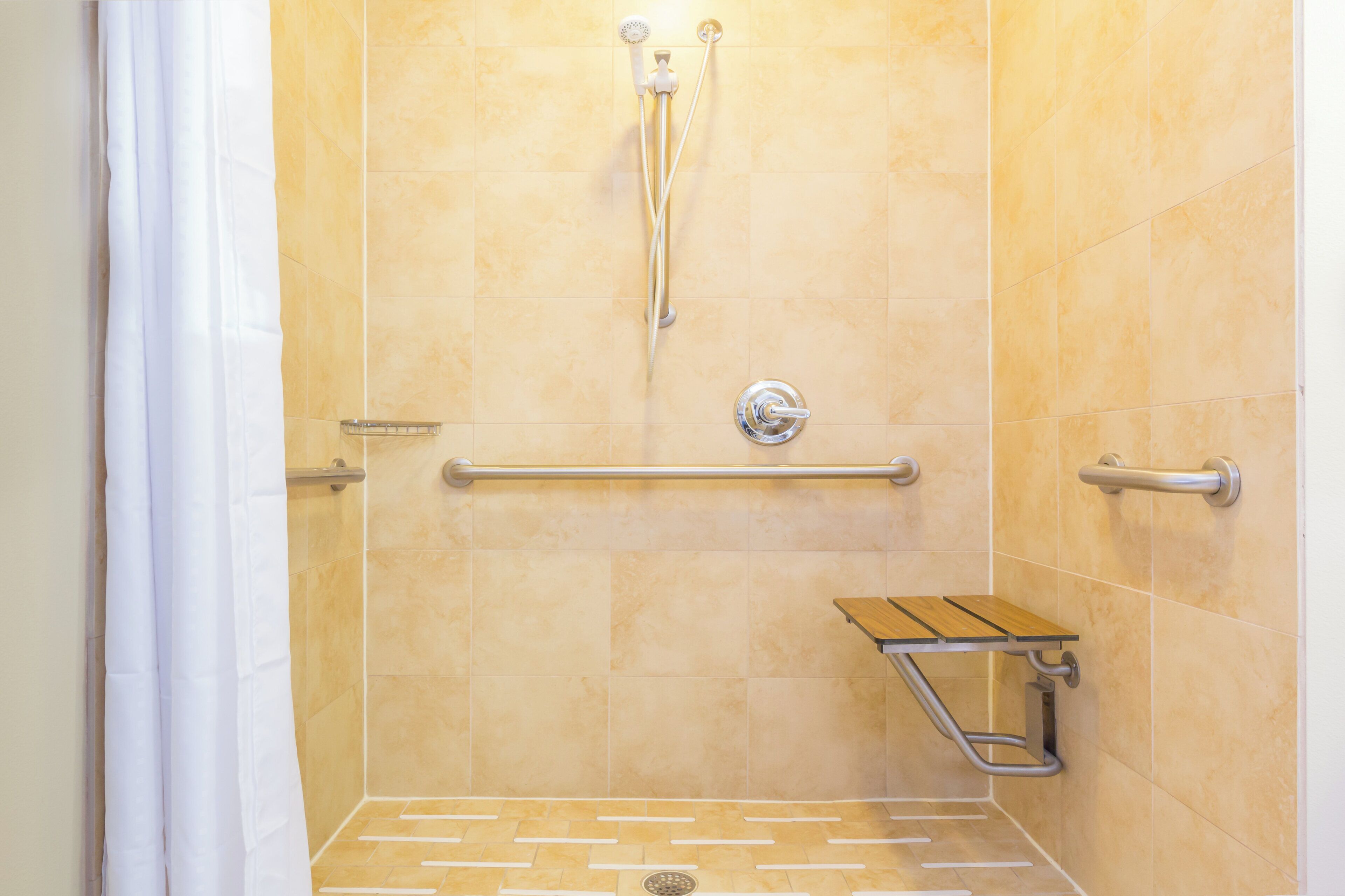 A shower area with a grab bar, a handheld showerhead, and a seat.