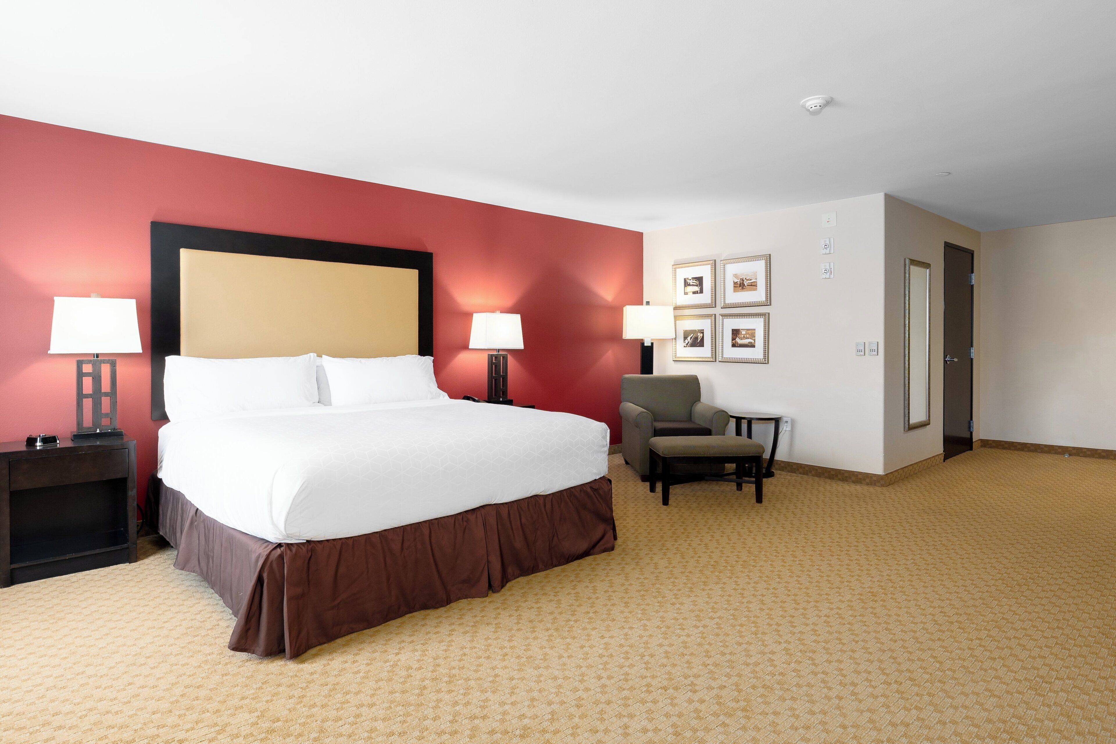 A hotel room with a large bed, two bedside tables with lamps, a chair, and a door.