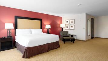 A hotel room with a large bed, two bedside tables with lamps, a chair, and a door.