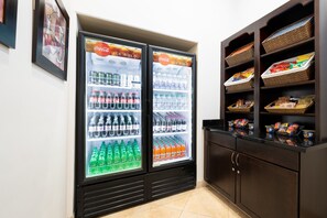 A room with two double-door refrigerators stocked with beverages and snacks, a dark wooden cabinet with baskets, and a framed picture on the wall.