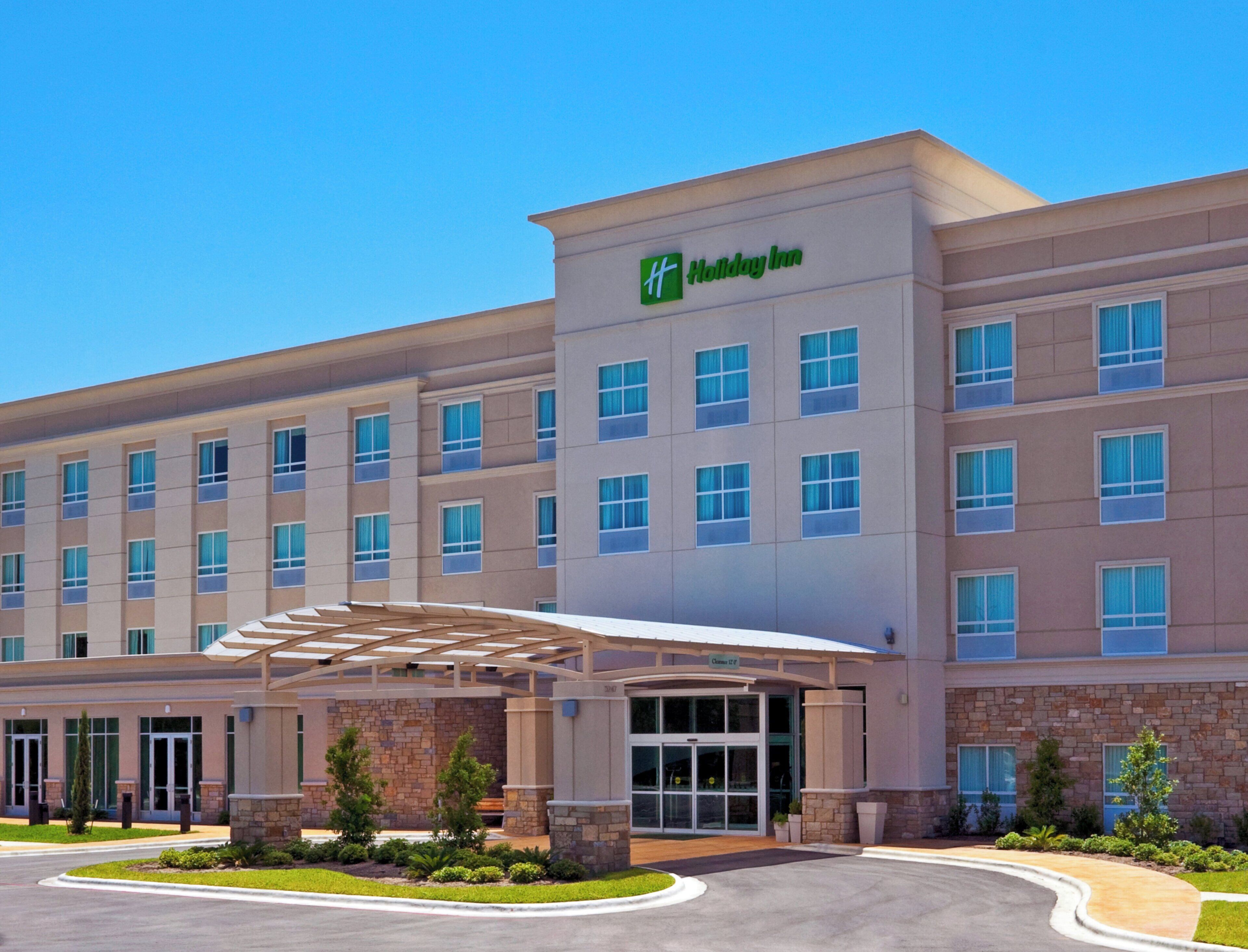 A Holiday Inn hotel with a covered entrance, multiple floors, and a clear sky.