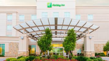 A Holiday Inn hotel with a covered entrance, multiple windows, and a landscaped garden with various plants and flowers.