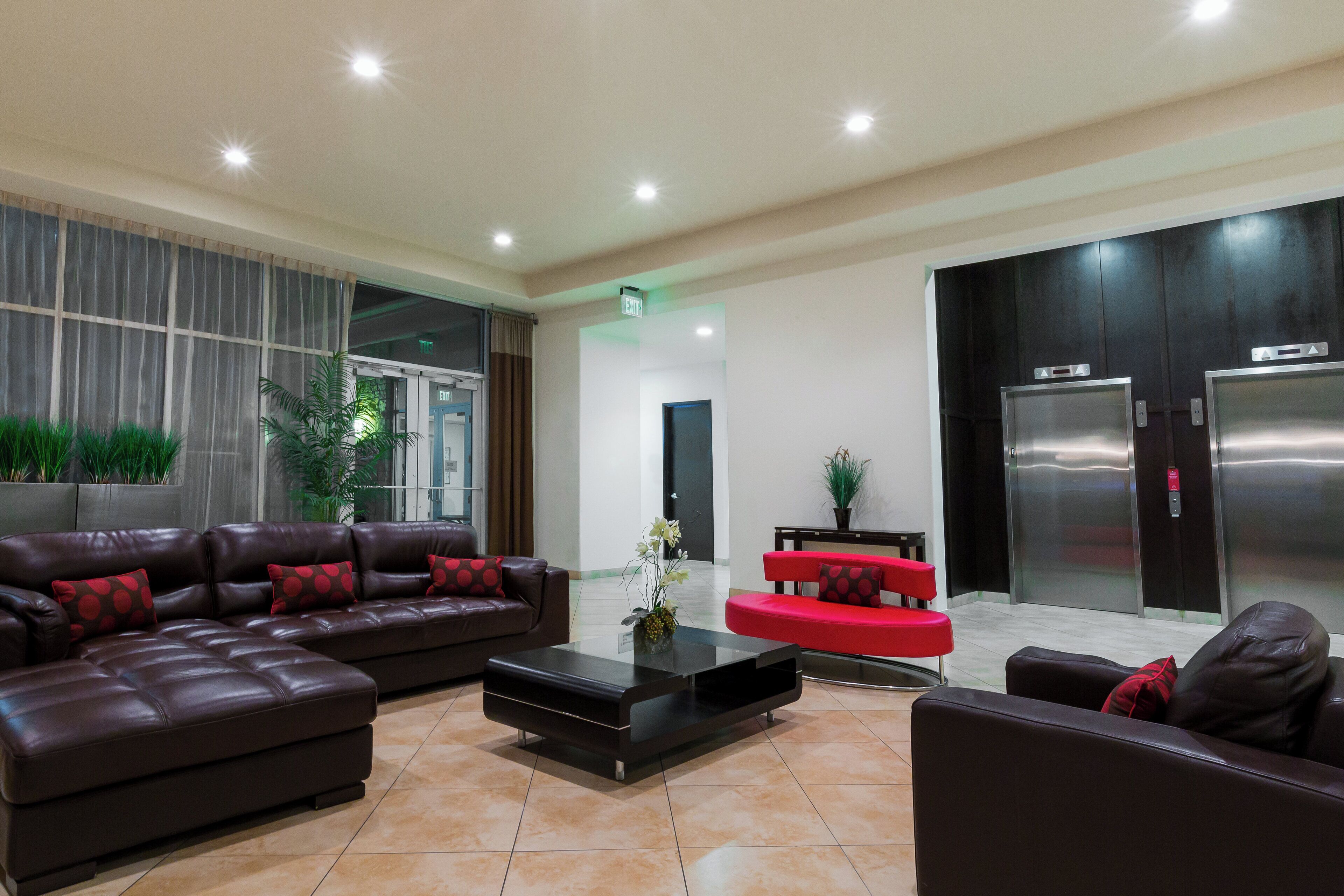 A lobby with a brown leather sofa, a red sofa, a coffee table, and an elevator.