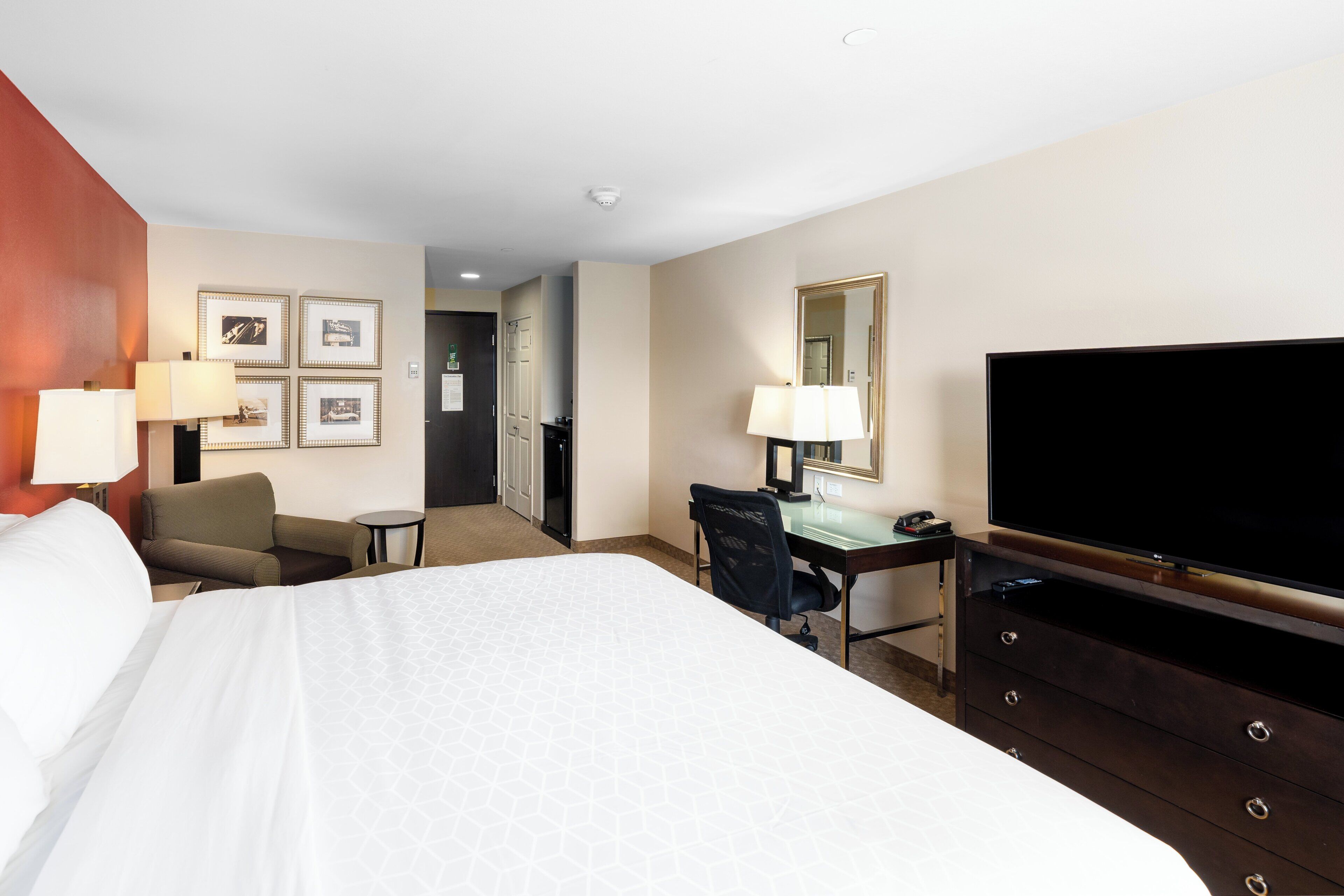 A hotel room with a bed, a desk, a chair, a television, and framed pictures on the wall.