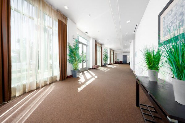 A spacious hallway with large windows, potted plants, and a wooden bench.