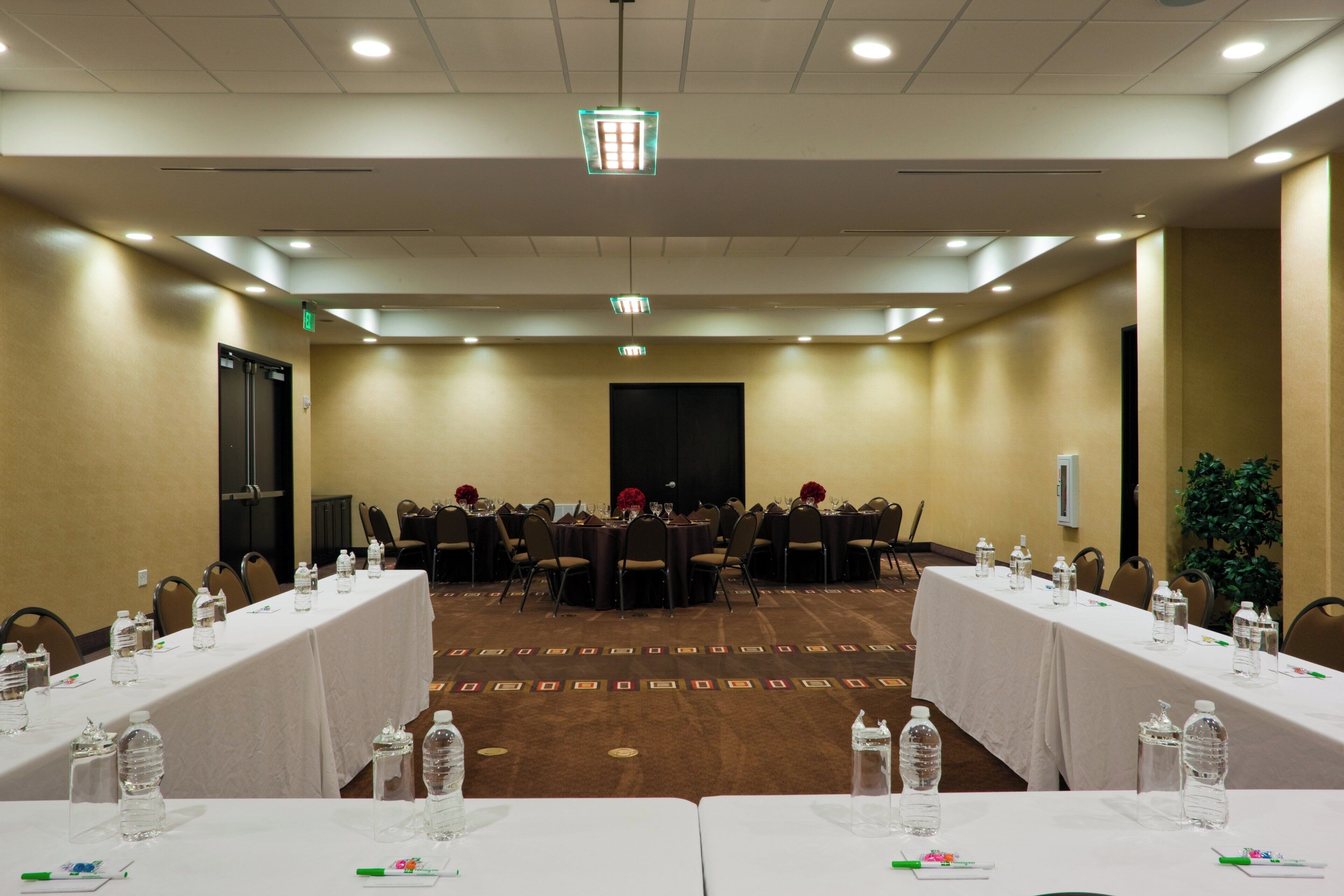 A conference room with tables, chairs, water bottles, and a large screen at the front.