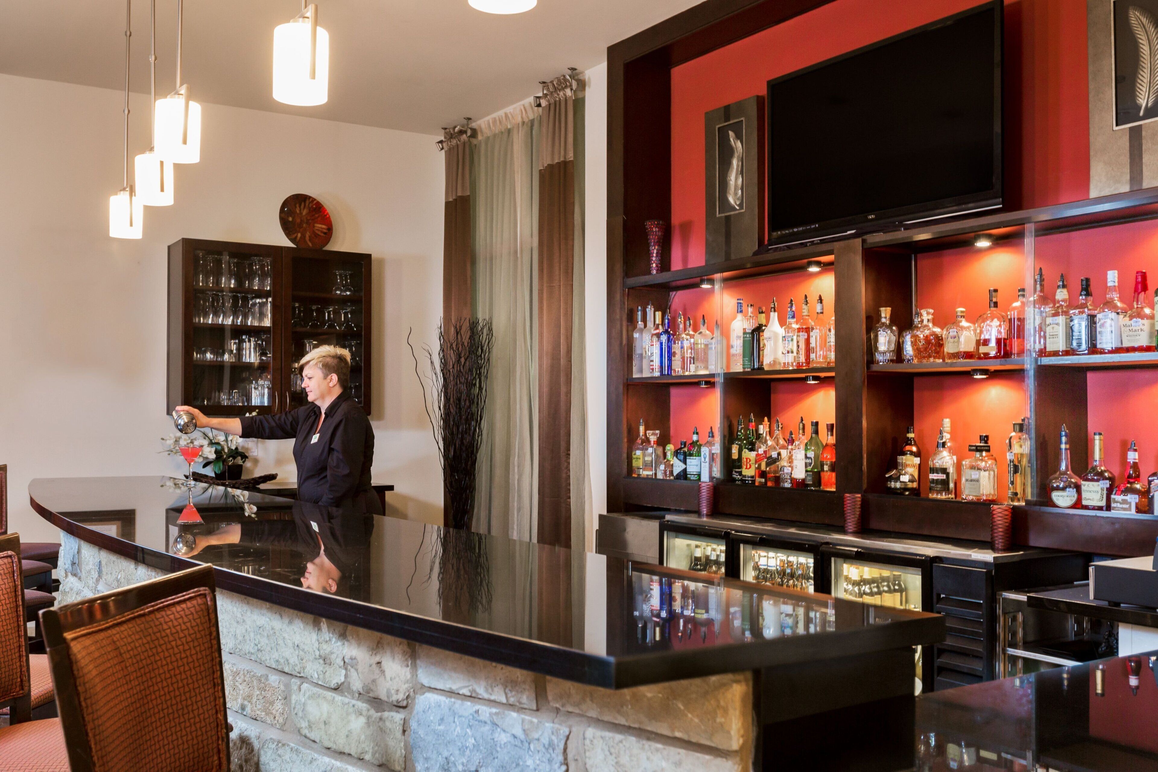 A bar area with a bartender, shelves of liquor bottles, and a television mounted on the wall.