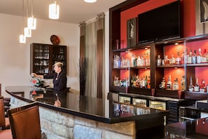 A bar area with a bartender, shelves of liquor bottles, a television, and a stone wall. - Holiday Inn Temple-Belton by IHG (Temple)