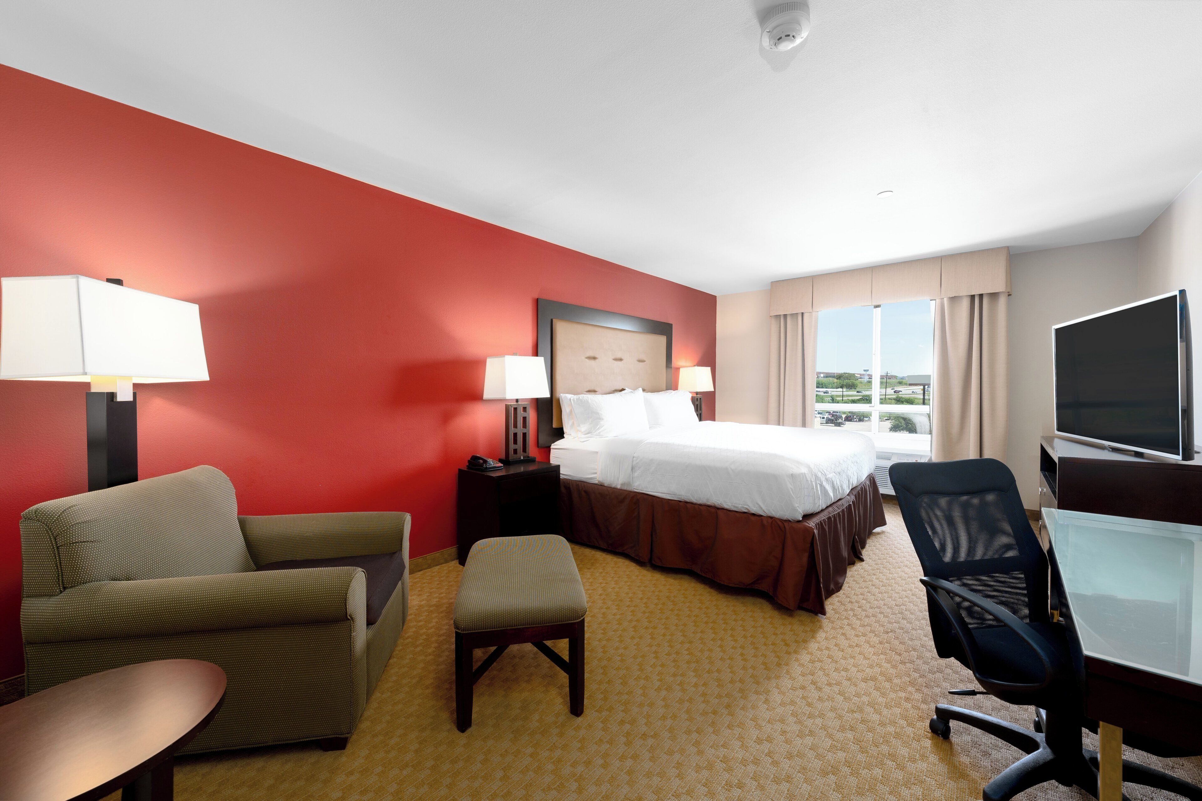 A hotel room with a bed, two chairs, a desk, a television, and a window with a view.