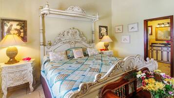 A four-poster bed with ornate headboard, two bedside tables with lamps, and a vase of flowers.