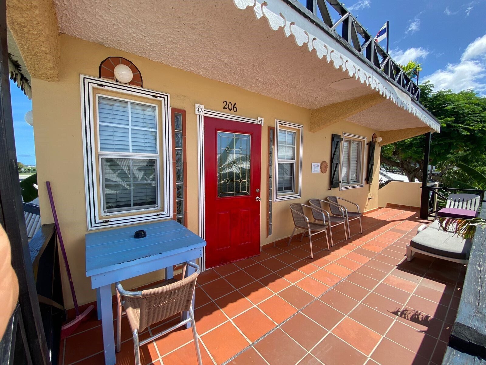 Un bâtiment avec une porte rouge, portant le numéro 206, et une table bleue avec des chaises à l’extérieur.