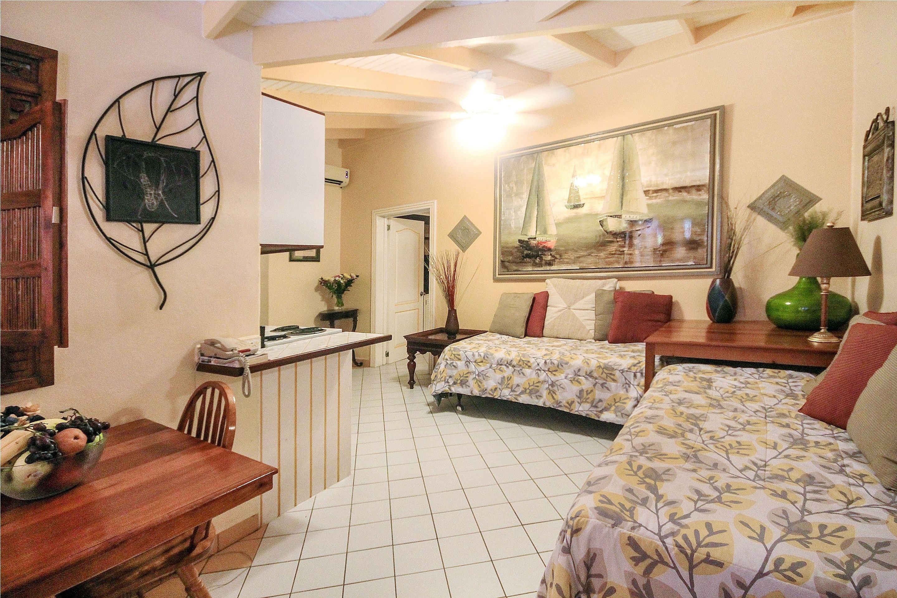 Habitación de hotel con dos camas, una mesa de comedor con frutero, un escritorio con teléfono y un amplio ventanal con un cuadro.