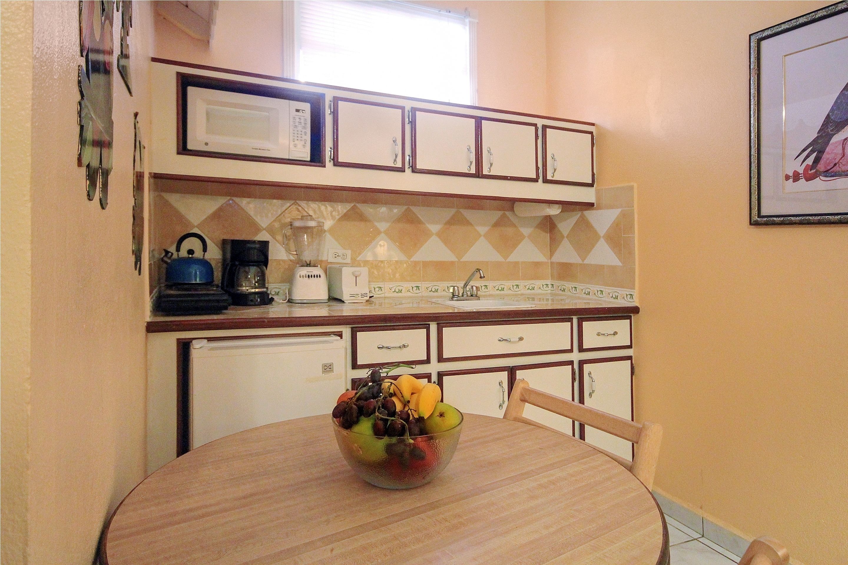 Una cocina con microondas, cafetera y un frutero sobre la mesa.