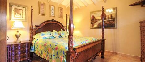 A four-poster bed with floral bedding, a wooden nightstand with a lamp, and a dresser with drawers.