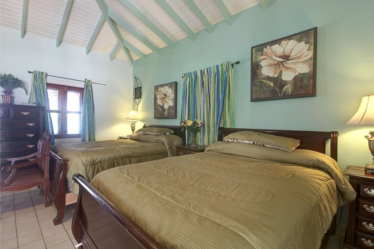 Quarto com duas camas, cômoda, cadeira e janela com cortinas.