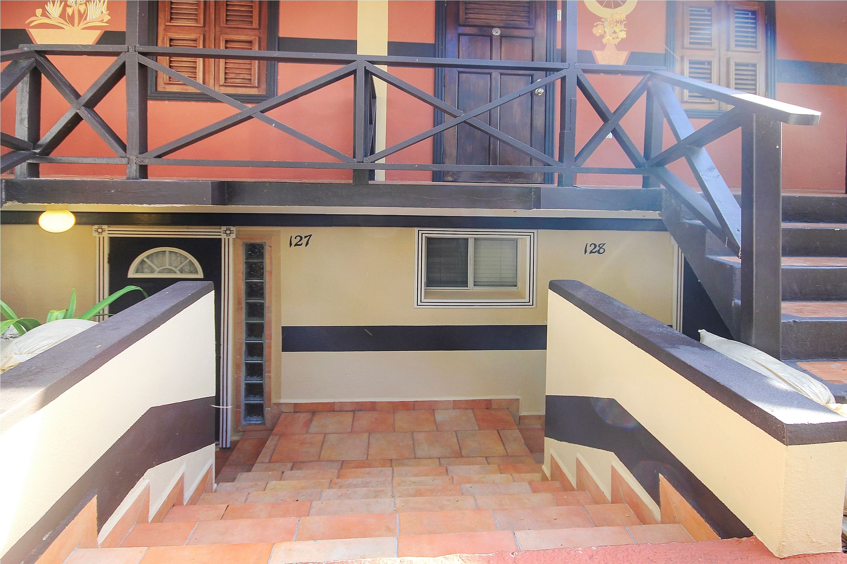Una escalera con barandilla, números 127 y 128 en las paredes, y un ventanal pequeño.