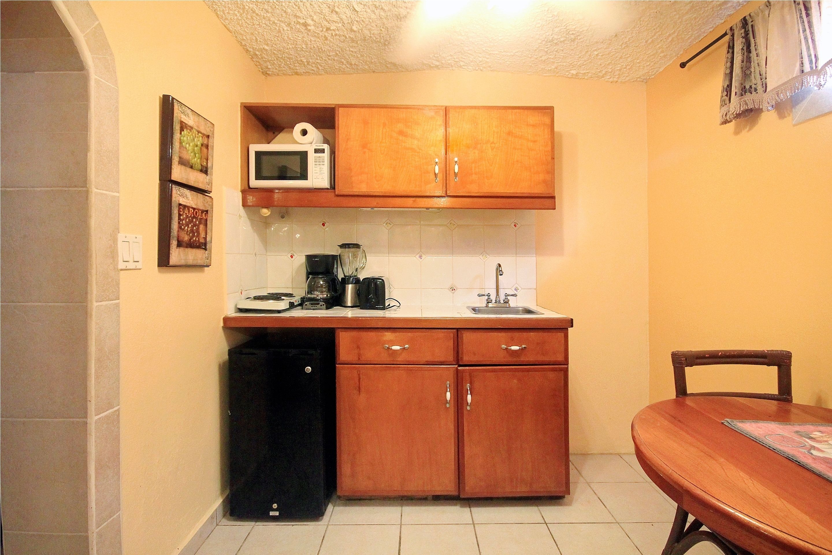 Una cocina compacta con armarios de madera, microondas, cafetera y un lavamanos.