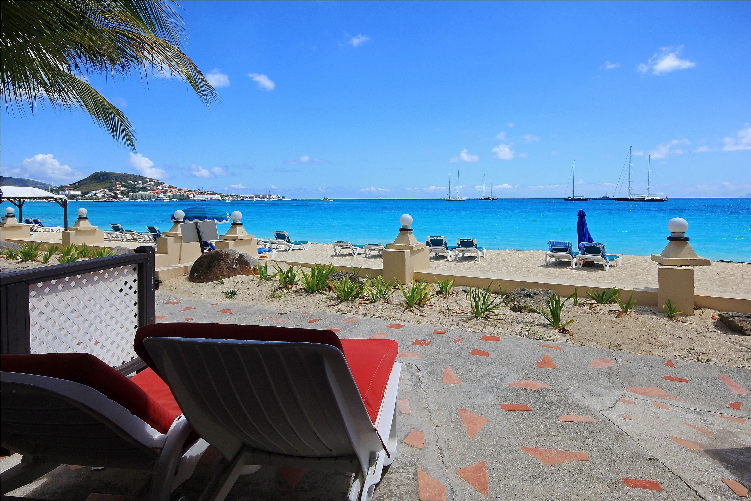 A beachside view with lounge chairs, a palm tree, and sailboats in the distance.