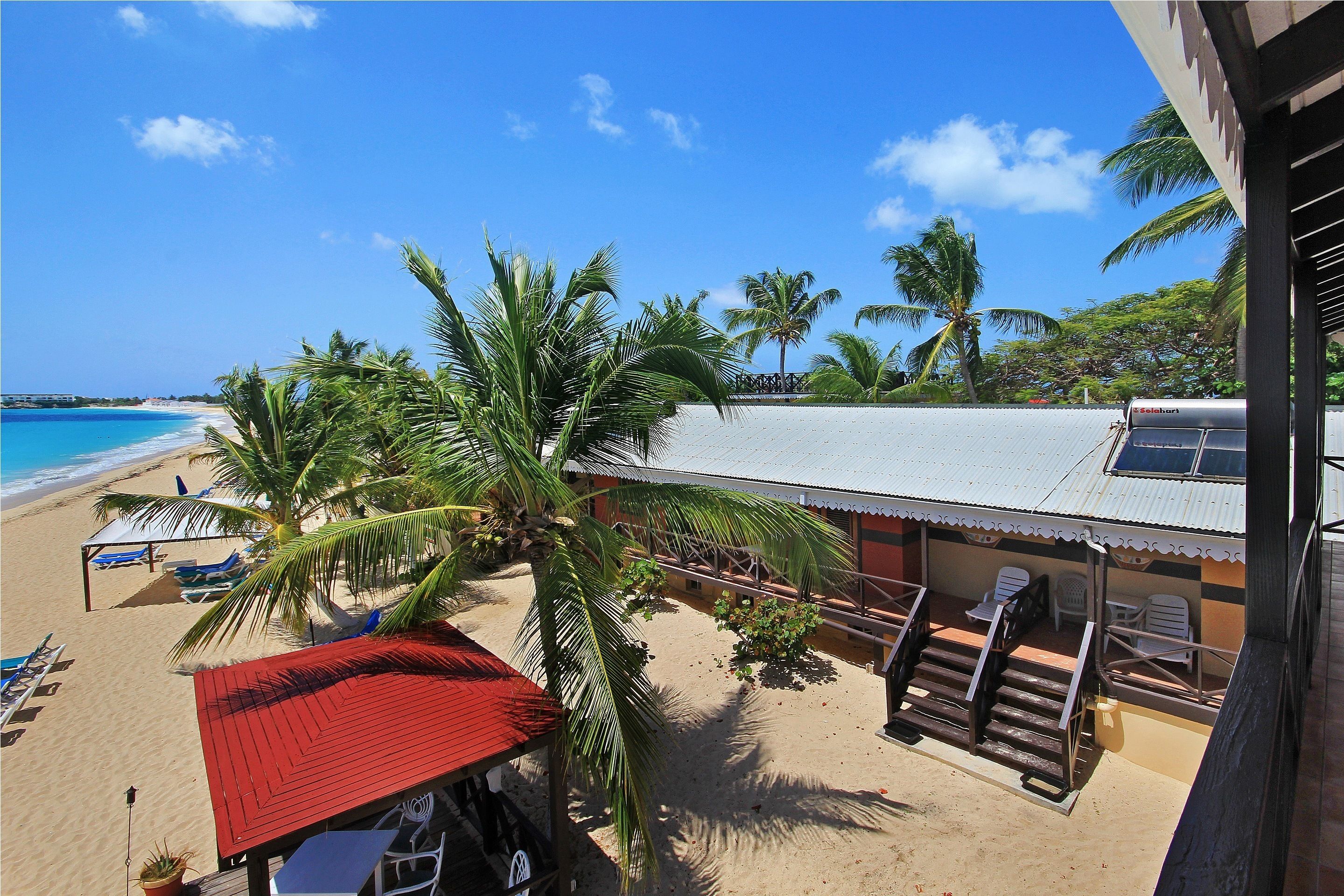 A beachside hotel with a red-roofed structure, a pool area with lounge chairs, and a view of the ocean.