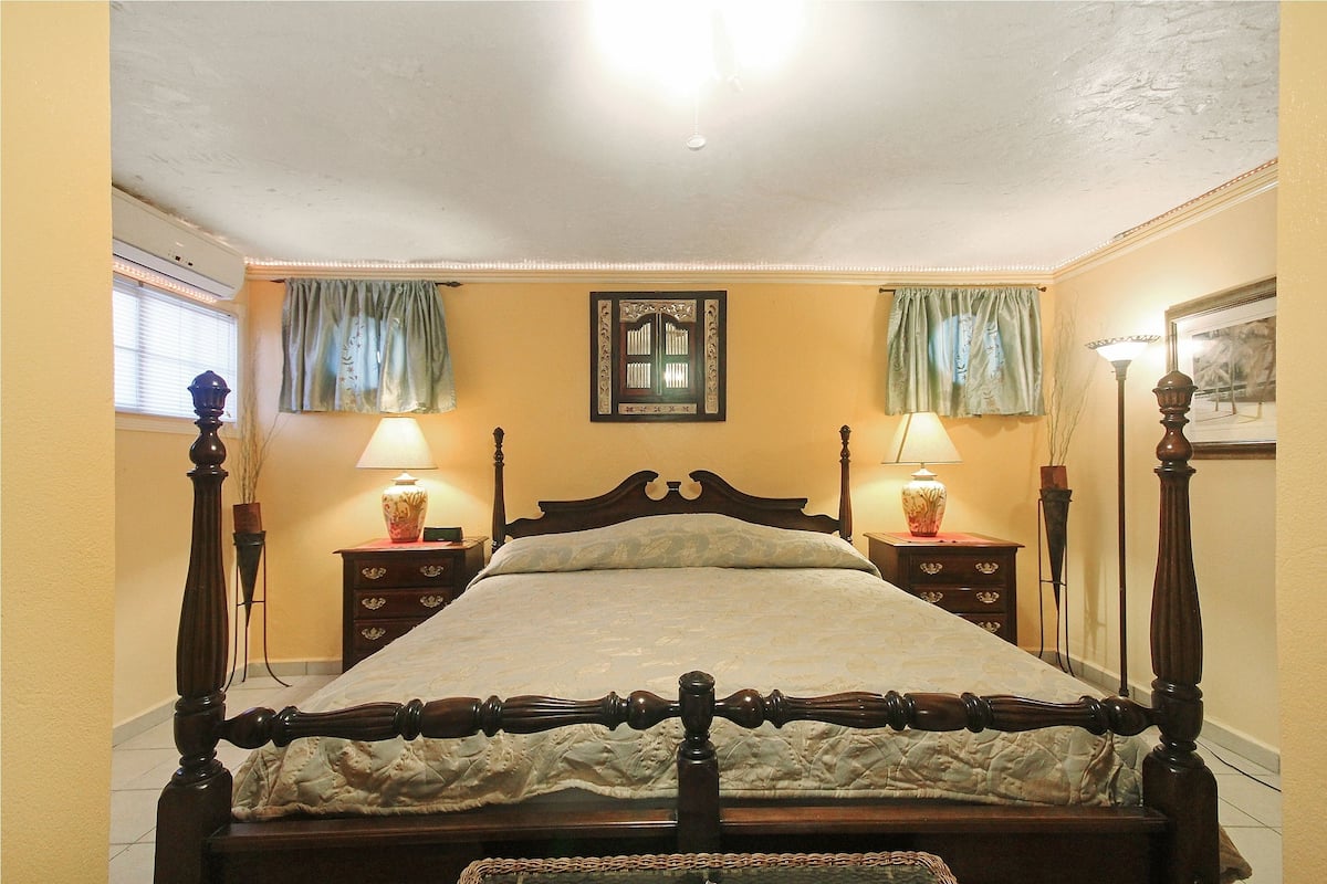 Quarto com uma cama de dossel de madeira, duas mesas de cabeceira com luminárias, uma janela com cortinas e um quadro na parede.