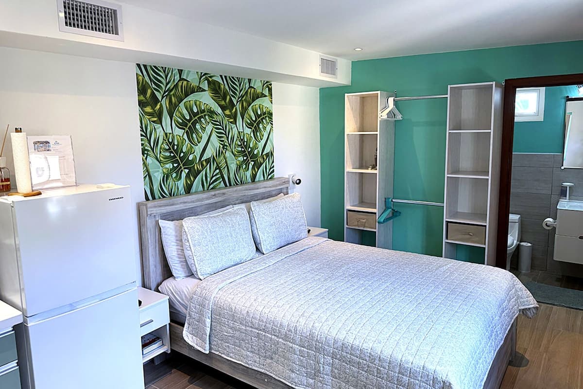 Quarto com cama, mesa de cabeceira, guarda-roupa e banheiro visível por uma porta aberta.