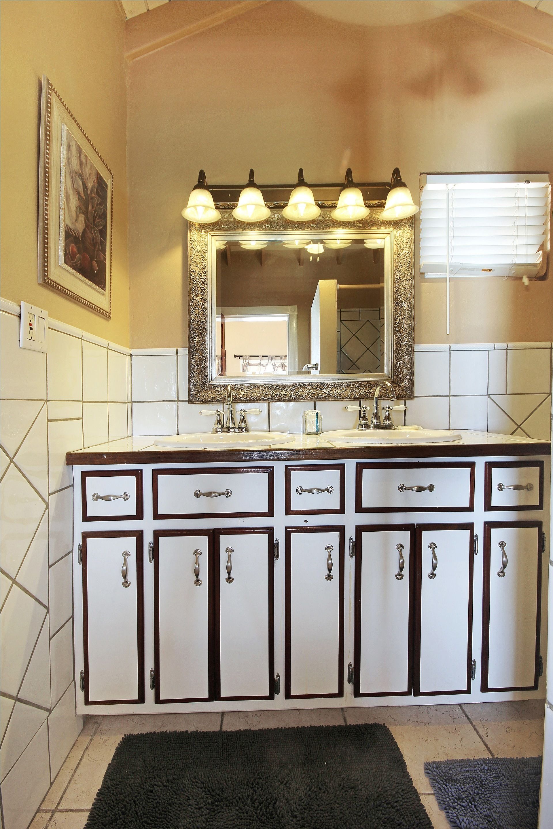 Un baño con un tocador amplio, un espejo con iluminación y una ventana con persianas.