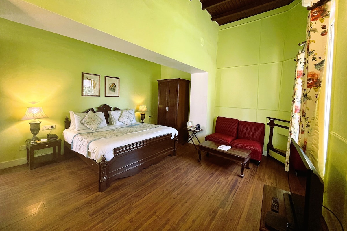 A room with a bed, a wooden cabinet, a red sofa, and a small table with a lamp.